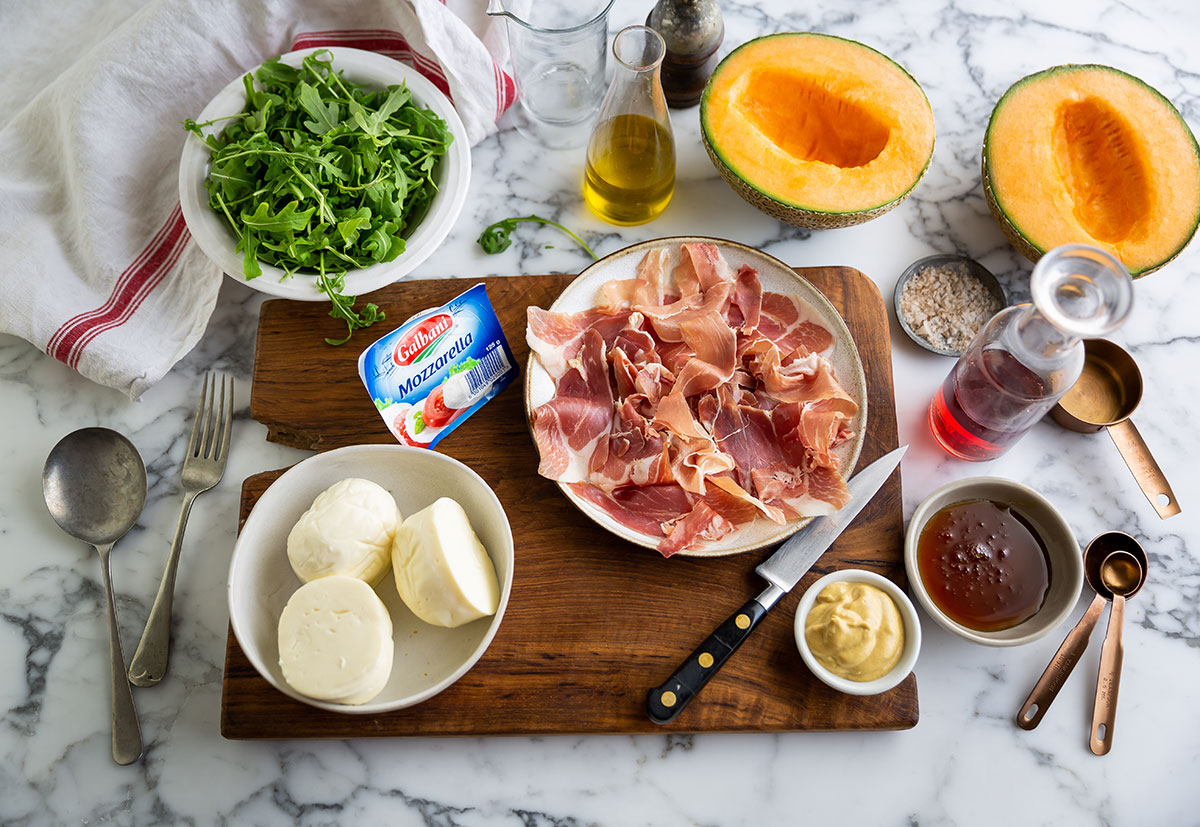 Ingrédients pour faire une salade de melon, mozzarella et jambon de parme disposés sur une planche